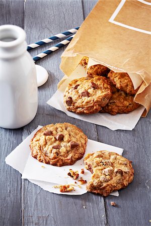 simsearch:600-09155531,k - Milk bottle and oatmeal chocolate chip cookies in a brown paper bag and a cookie with a bite taken out of it with crumbs Foto de stock - Sin royalties Premium, Código: 600-09155487