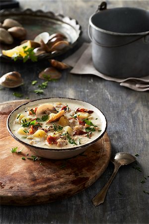 Bowl of clam chowder on a cutting board with ingredients in the background on a grey, wooden table Stock Photo - Premium Royalty-Free, Code: 600-09155504