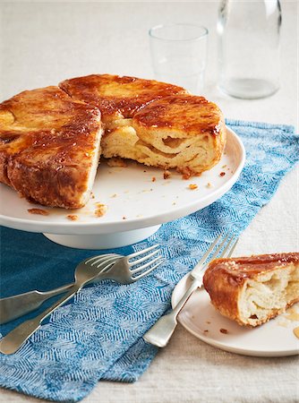 Kouign Amann on a cake stand with a piece taken out and served on dessert plate with forks in front Stock Photo - Premium Royalty-Free, Code: 600-09155508