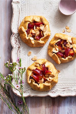 Three plum almond galettes on a decorative, rustic serving tray with purple flowers Stock Photo - Premium Royalty-Free, Code: 600-09155511