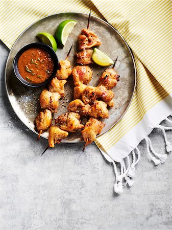 Chicken satay skewers with dipping sauce and lime wedges on a metal tray on striped fabric Stockbilder - Premium RF Lizenzfrei, Bildnummer: 600-09155562