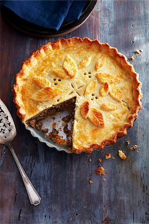 simsearch:400-07625362,k - Tourtiere with a decorated crust and one piece taken out on a blue wooden background Stock Photo - Premium Royalty-Free, Code: 600-09155601