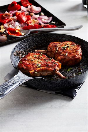 simsearch:600-09155590,k - Glazed pork chops in a cast iron skillet with roasted vegetables in the background Stock Photo - Premium Royalty-Free, Code: 600-09159789