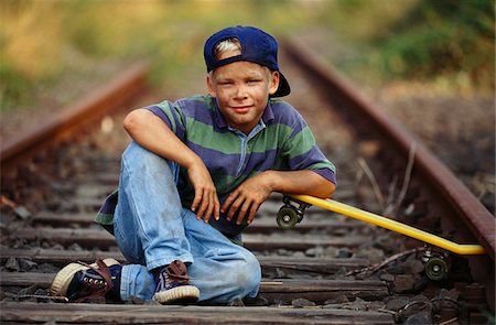 Boy With Skateboard Sitting On Train Tracks Stock Photo - Premium Royalty-Free, Code: 600-00948338