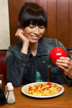 french fry smile - Woman Pouring Ketchup on French Fries Stock Photo - Premium Royalty-Free, Code: 600-01042065
