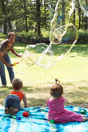 dad baby playing toy - Father Blowing Bubbles while Babies Watch Stock Photo - Premium Royalty-Free, Code: 600-01073153