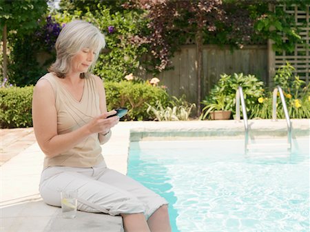 simsearch:600-03586419,k - Femme à côté de la piscine à la recherche de la PDA Photographie de stock - Premium Libres de Droits, Code: 600-01084274