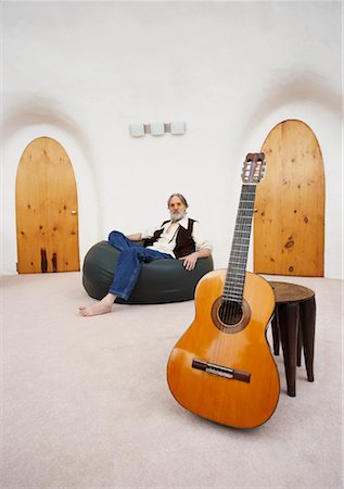 Man Sitting in Bean Bag Chair with Guitar in Foreground Foto de stock - Royalty Free Premium, Número: 600-01083729