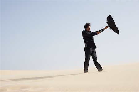 Homme d'affaires dans le désert avec parapluie balayées par le vent Photographie de stock - Premium Libres de Droits, Code: 600-01110014