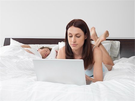 Woman Using Laptop Computer in Bed while Man Sleeps Photographie de stock - Premium Libres de Droits, Code: 600-01295818