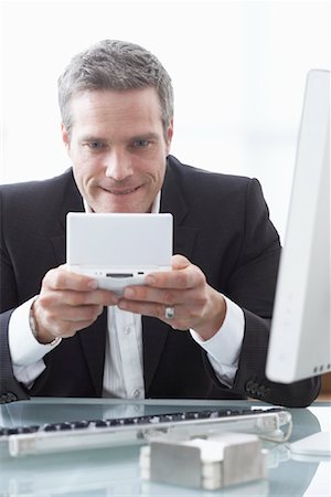 simsearch:600-02081740,k - Businessman Playing Handheld Video Game at Desk Foto de stock - Royalty Free Premium, Número: 600-02081703