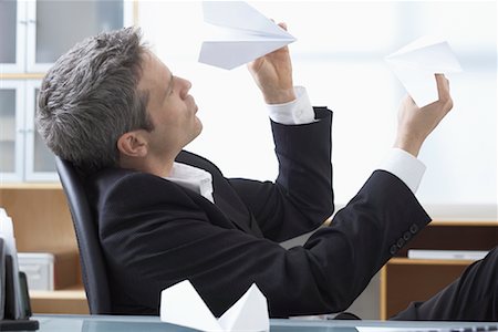 Businessman Playing with Paper Airplanes at Desk Foto de stock - Sin royalties Premium, Código: 600-02081710