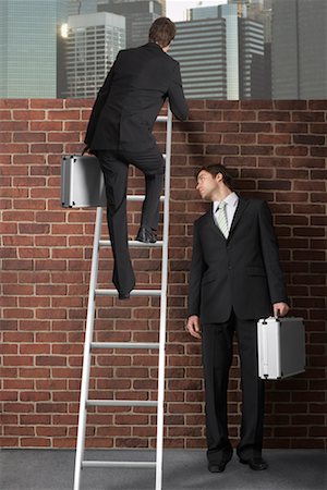 superação de obstáculos - Businessman Climbing Ladder Over Brick Wall While Other Businessman Looks On Foto de stock - Royalty Free Premium, Número: 600-02315974