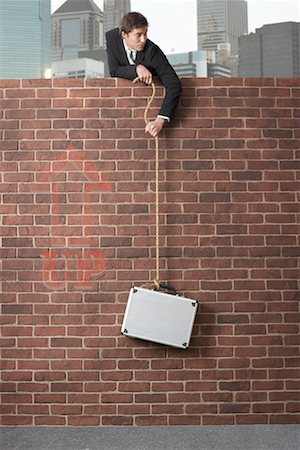 Businessman Lowering Briefcase Over Brick Wall Stock Photo - Premium Royalty-Free, Code: 600-02312388