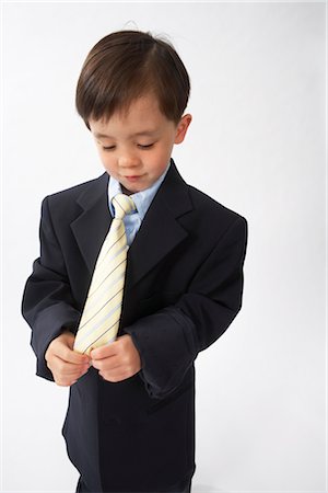 Little Boy Dressed Up as a Businessman Looking at His Tie Stock Photo - Premium Royalty-Free, Code: 600-02693720