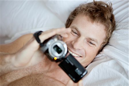 Man Lying in Bed Holding a Video Camera Fotografie stock - Premium Royalty-Free, Codice: 600-02757321