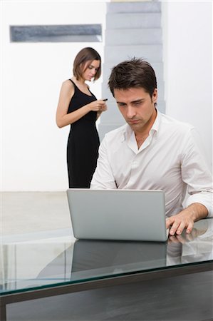 simsearch:614-02680155,k - Businessman Using Laptop Computer, Businesswoman in the Background With Cell Phone Stock Photo - Premium Royalty-Free, Code: 600-03520614