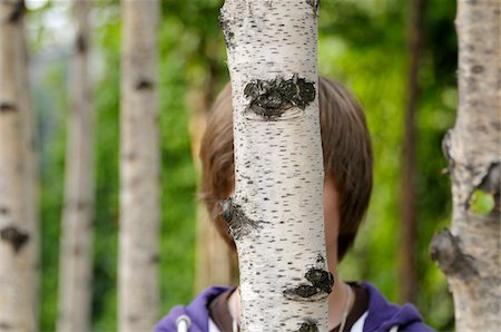 Boy Hidden Behind Tree trunk Foto de stock - Sin royalties Premium, Código: 600-03836149