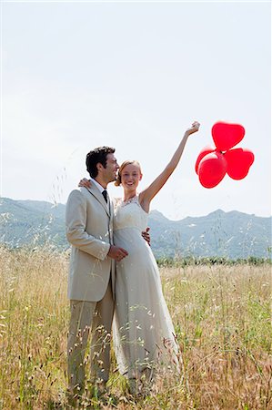 Newlyweds in field with red heart shape balloons Stock Photo - Premium Royalty-Free, Code: 614-05399381