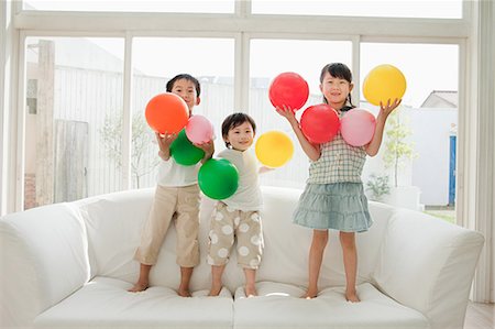 siblings - Three children standing on sofa with balloons Stock Photo - Premium Royalty-Free, Code: 614-05399835