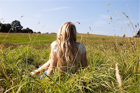 Young woman sitting in a field with back to camera Stock Photo - Premium Royalty-Free, Code: 614-05557076