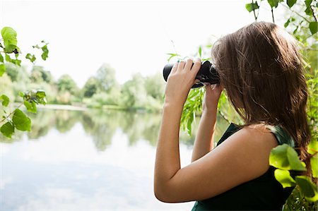 spying person - Young woman looking through binoculars across a lake Stock Photo - Premium Royalty-Free, Code: 614-05557111