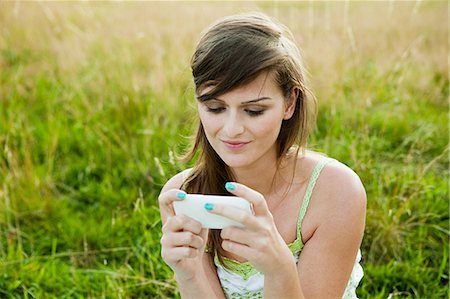 Young woman looking at a hand held device in a field Stock Photo - Premium Royalty-Free, Code: 614-05557124