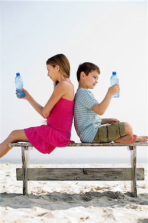 sister back to back - Girl and boy holding bottles of water on a beach Stock Photo - Premium Royalty-Free, Code: 614-05557176