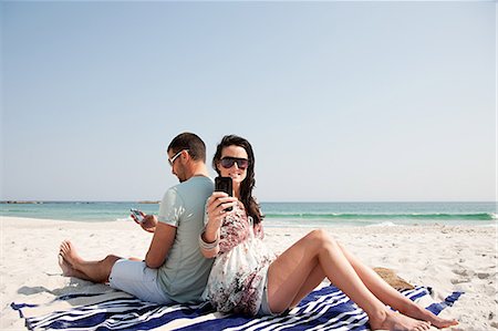 Séance de couple dos à dos sur une plage en utilisant les téléphones mobiles Photographie de stock - Premium Libres de Droits, Code: 614-05557188