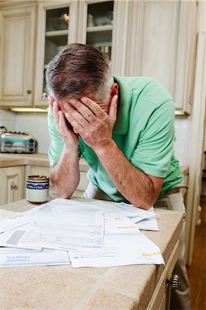 Mature man with head in hands over table of household bills Stock Photo - Premium Royalty-Free, Code: 614-05557354