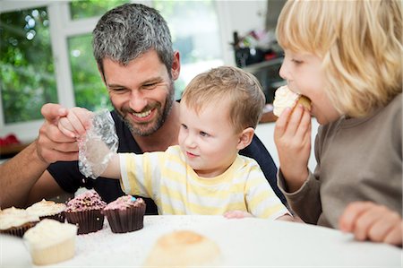 parents and children and cupcakes - Mid adult man decorating cupcakes with his sons Stock Photo - Premium Royalty-Free, Code: 614-05557426