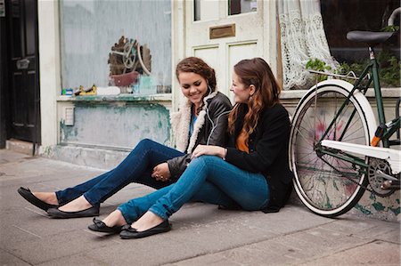 Two young women sitting on pavement outside cafe Stock Photo - Premium Royalty-Free, Code: 614-05662134