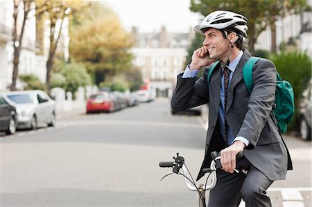 Mid adult businessman using cellphone on bicycle Foto de stock - Sin royalties Premium, Código: 614-05662304