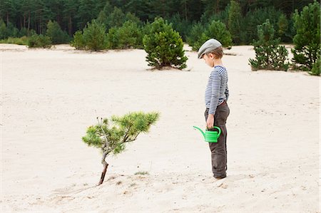 Boy with watering can, looking at plant in sand Stock Photo - Premium Royalty-Free, Code: 614-05955512