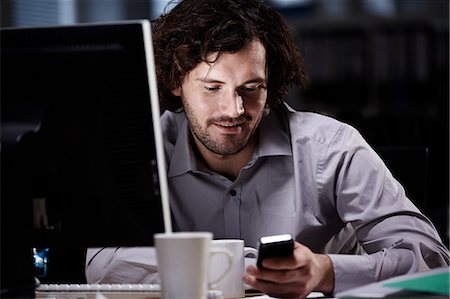 person smiling desk alone - Office worker looking at cellphone in dark office Stock Photo - Premium Royalty-Free, Code: 614-05955705