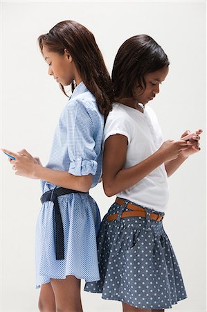 sister back to back - African American sisters using cellphones, studio shot Stock Photo - Premium Royalty-Free, Code: 614-06002419