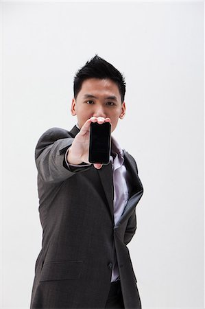 portrait young adult front - Young Asian businessman holding cellphone, studio shot Stock Photo - Premium Royalty-Free, Code: 614-06002451