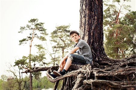 Boy sitting on roots of tree trunk Stock Photo - Premium Royalty-Free, Code: 614-06116046
