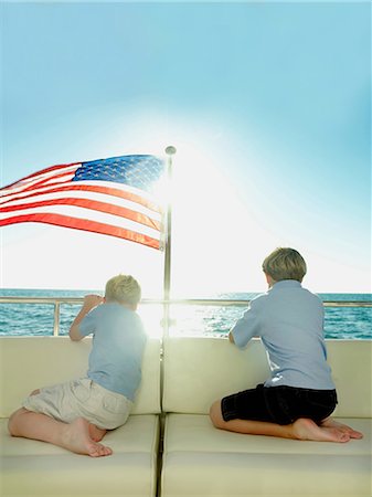 Boys in the back of a yacht with american flag, looking out to sea Stock Photo - Premium Royalty-Free, Code: 614-06116402