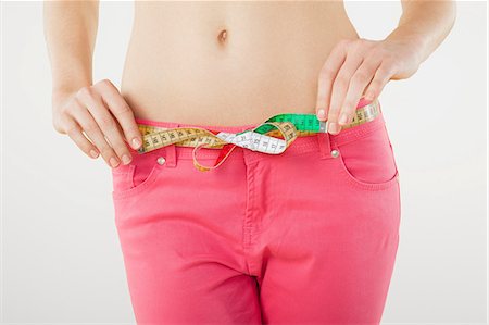 front view - Young woman measuring waist with tape measure Stock Photo - Premium Royalty-Free, Code: 614-06168642