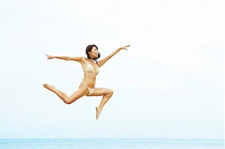 Young woman in bikini jumping on beach Stock Photo - Premium Royalty-Free, Code: 614-06169382