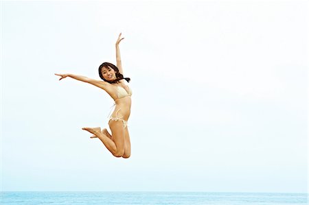Young woman in bikini jumping on beach Stock Photo - Premium Royalty-Free, Code: 614-06169383