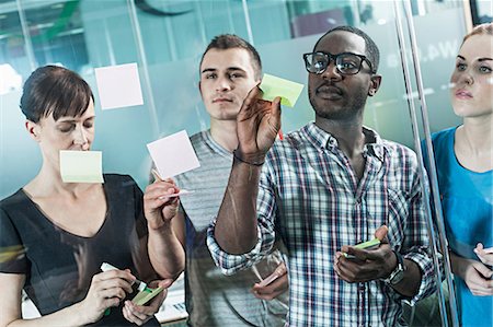 sticky note - Colleagues writing on adhesive notes and sticking them to window Stock Photo - Premium Royalty-Free, Code: 614-06311944