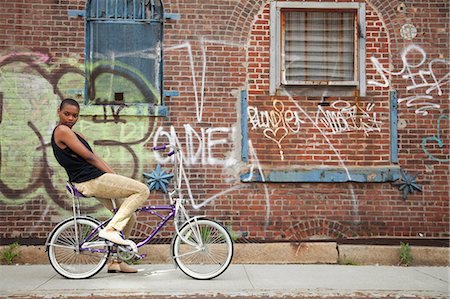 Portrait of a young woman on bicycle by wall covered in graffiti Stock Photo - Premium Royalty-Free, Code: 614-06311992