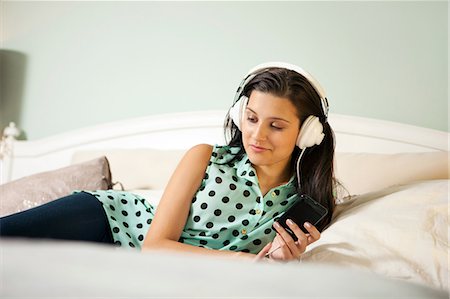 Young woman on bed wearing earphones Stock Photo - Premium Royalty-Free, Code: 614-06335998