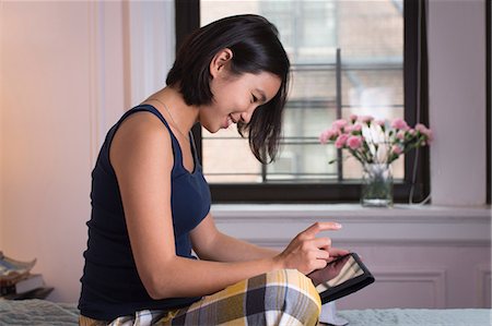 Young woman sitting on bed, using digital tablet Stock Photo - Premium Royalty-Free, Code: 614-06336138