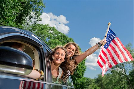 Two friends leaning out of car window holding american flag Foto de stock - Sin royalties Premium, Código: 614-06402503