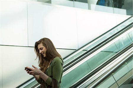 Young woman on escalator using smartphone Stock Photo - Premium Royalty-Free, Code: 614-06402754