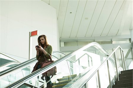 scala mobile - Young woman on escalator using smartphone Fotografie stock - Premium Royalty-Free, Codice: 614-06402753