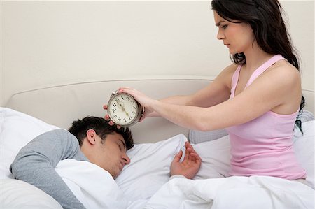 entre 20 y 30 años - Couple in bed, woman holding alarm clock near mans head Foto de stock - Sin royalties Premium, Código: 614-06442421